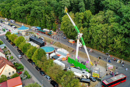 Forchheim Germany 25 July 2025 Aerial view of the Annafest fairground with amusement rides crowds of people and a red bus next to a lush forest. Forchheim Germany 25 July 2025 Aerial view of the Annafest fairground with amusement rides crowds of people and a red bus next to a lush forest.