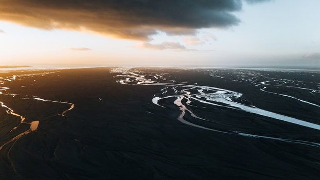 Aerial view of a braided glacial river system flowing through black volcanic sand under a dramatic sunset sky in Skaftarhreppur Iceland.