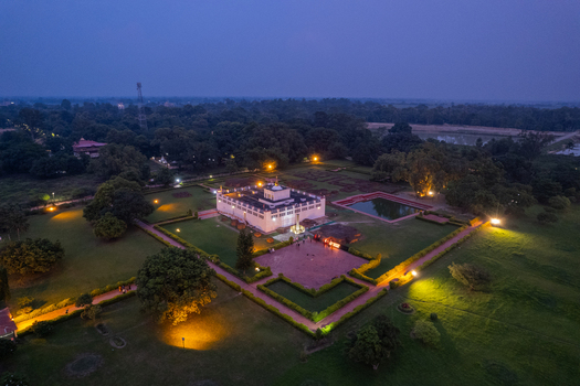 Aerial view of the Maya Devi Temple in Lumbini illuminated at dusk surrounded by lush gardens and pathways in Nepal.