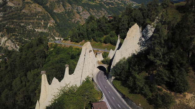Aerial view of the Pyramides d Euseigne rock formations and a winding mountain road passing through the alpine forest in Heremence Valais Switzerland. Aerial view of the Pyramides d Euseigne rock formations and a winding mountain road passing through the alpine forest in Heremence Valais Switzerland.