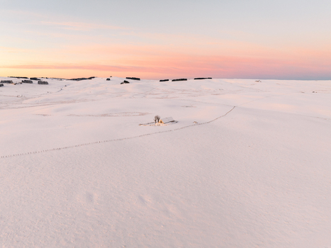 Aerial view of a snow covered landscape kissed by the soft hues of dawn with distant structures adding a touch of mystery Nasbinals Occitanie France.