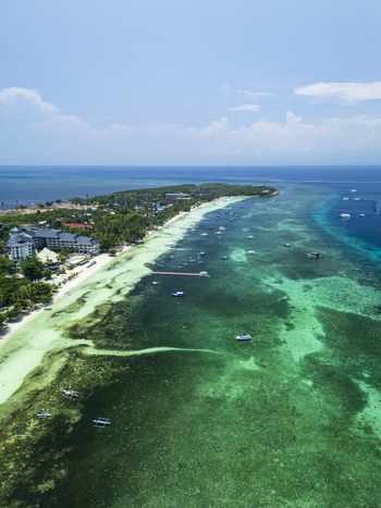 Aerial view of the Doljo coastline featuring a luxury resort turquoise waters scattered boats and coral reefs in Panglao Central Visayas Philippines.