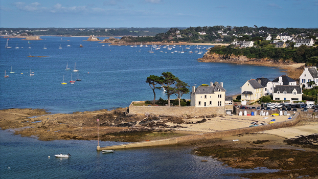Aerial view of the rugged coastline meeting the serene waters boats dotting the bay under a clear sky Carantec Brittany France.