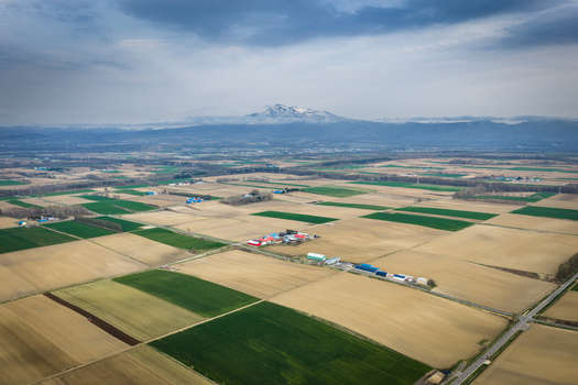 Aerial view of the agricultural landscape near Lake Kussharo featuring patchwork fields farm buildings and distant snow capped mountains under a cloudy sky in Teshikaga Hokkaido Japan. Aerial view of the agricultural landscape near Lake Kussharo featuring patchwork fields farm buildings and distant snow capped mountains under a cloudy sky in Teshikaga Hokkaido Japan.