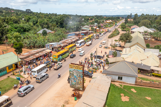 Aerial view of the busy road in Lukaya with buses cars and pedestrians passing by roadside shops and green vegetation in Lukaya Central Region Uganda.