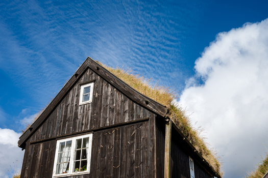 View of a traditional wooden house with a grass roof under a bright blue sky in the Faroe Islands. View of a traditional wooden house with a grass roof under a bright blue sky in the Faroe Islands.