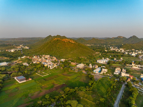 Aerial view of the lush green landscape surrounding the city of Udaipur featuring rolling hills agricultural fields and scattered residential buildings in Udaipur Rajasthan India.