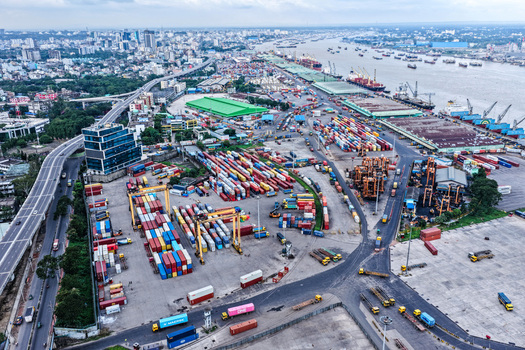 Aerial view of Chattogram Port featuring rows of colorful shipping containers gantry cranes and cargo ships docked along the river in Chittagong Chittagong Division Bangladesh.