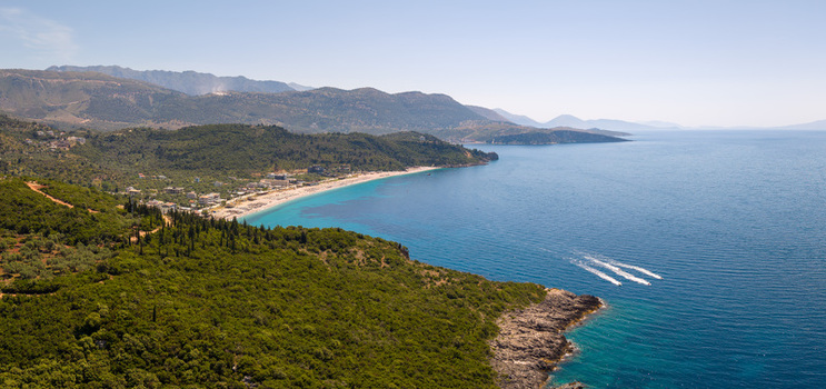 Aerial view of Aquarium Beach with turquoise waters lush green hills and boats on the blue sea in Jala Vlore County Albania.
