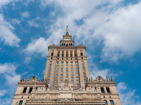 View of the Palace of Culture and Science with its ornate stone facade and central spire against a bright blue sky with scattered clouds in Warszawa Wojewodztwo mazowieckie Poland. View of the Palace of Culture and Science with its ornate stone facade and central spire against a bright blue sky with scattered clouds in Warszawa Wojewodztwo mazowieckie Poland.