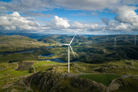 Aerial view of Makaknuten Vindkraftverk wind turbine on a hilly landscape with lakes and green fields under a cloudy blue sky in Bjerkreim Municipality Rogaland Norway. Aerial view of Makaknuten Vindkraftverk wind turbine on a hilly landscape with lakes and green fields under a cloudy blue sky in Bjerkreim Municipality Rogaland Norway.