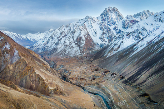 Aerial view of the rugged snow capped peaks towering over the arid valley floor where a thin ribbon of river carves through the landscape Hunza Nagar Gilgit Pakistan. Aerial view of the rugged snow capped peaks towering over the arid valley floor where a thin ribbon of river carves through the landscape Hunza Nagar Gilgit Pakistan.