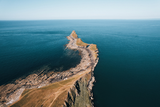 Aerial view of Worms Head Causeway extending into the sea with rugged rocky cliffs and grassy headlands in Rhossili Wales United Kingdom.