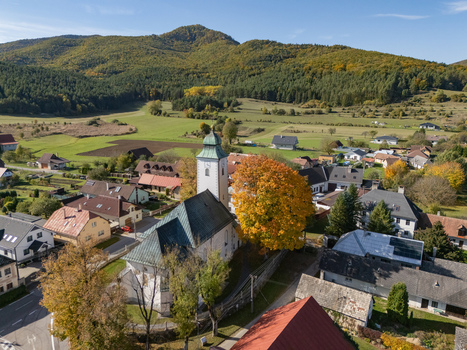Aerial view of a village church with a green spire and a brilliant autumn tree amidst homes and dark green hills Klastor pod Znievom Zilina Region Slovakia. Aerial view of a village church with a green spire and a brilliant autumn tree amidst homes and dark green hills Klastor pod Znievom Zilina Region Slovakia.