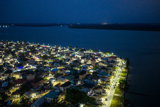 Aerial view of the illuminated coastal town of Opobo Town at night featuring glowing streetlights buildings and dark river waters along the shoreline in Opobo Town Rivers Nigeria. Aerial view of the illuminated coastal town of Opobo Town at night featuring glowing streetlights buildings and dark river waters along the shoreline in Opobo Town Rivers Nigeria.