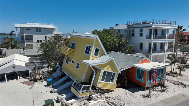 Aerial view of a damaged yellow house tilted on its foundation after a storm with debris and nearby coastal homes in Bradenton Beach Florida United States. Aerial view of a damaged yellow house tilted on its foundation after a storm with debris and nearby coastal homes in Bradenton Beach Florida United States.