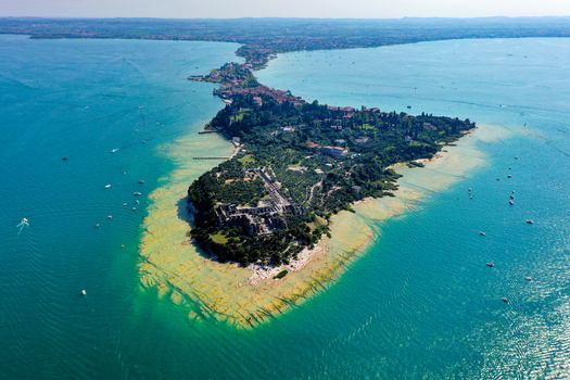 Aerial view of the Grotte di Catullo Roman ruins at the tip of the Sirmione peninsula surrounded by the turquoise waters of Lake Garda in Sirmione Lombardia Italy. Aerial view of the Grotte di Catullo Roman ruins at the tip of the Sirmione peninsula surrounded by the turquoise waters of Lake Garda in Sirmione Lombardia Italy.
