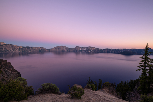 View of the deep still waters reflecting the pastel sky as the rugged cliffs stand guard in the serene twilight Crater Lake Oregon United States. View of the deep still waters reflecting the pastel sky as the rugged cliffs stand guard in the serene twilight Crater Lake Oregon United States.