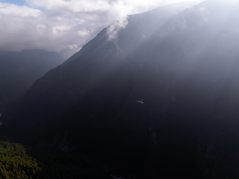 Aerial view of a helicopter flying over the rugged misty mountains of the Himalayas in Nepal.