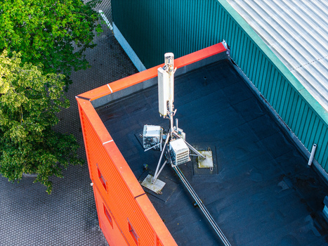 Aerial view of a cellular antenna base station mounted on a flat rooftop with an orange facade and green metal roof section in Riga Latvia. Aerial view of a cellular antenna base station mounted on a flat rooftop with an orange facade and green metal roof section in Riga Latvia.