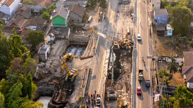 Indonesia 24 September 2026 Aerial view of road construction showing excavators cranes and workers on a busy street with traffic surrounded by residential houses and lush trees.