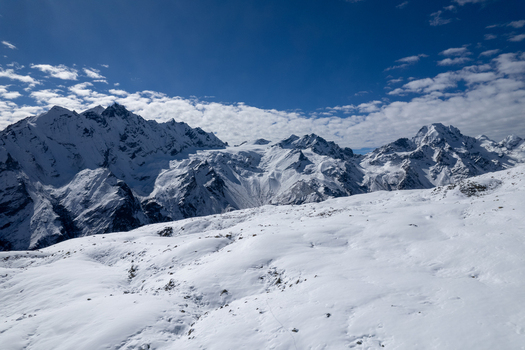 Aerial view of snow covered Himalayan peaks under a bright blue sky with scattered clouds in Nepal.