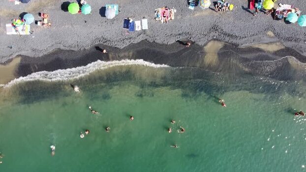 Aerial view of people on a dark sand beach with turquoise water Italy. Aerial view of people on a dark sand beach with turquoise water Italy.