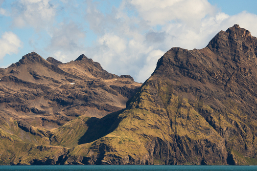 View of Jason Harbour with rugged mountain peaks and rocky coastline under a cloudy sky in South Georgia and the South Sandwich Islands. View of Jason Harbour with rugged mountain peaks and rocky coastline under a cloudy sky in South Georgia and the South Sandwich Islands.