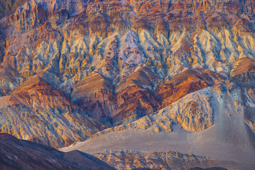 View of the colorful layered rock formations of Death Valley National Park featuring vibrant mineral deposits and rugged desert terrain illuminated by golden hour light in the United States.