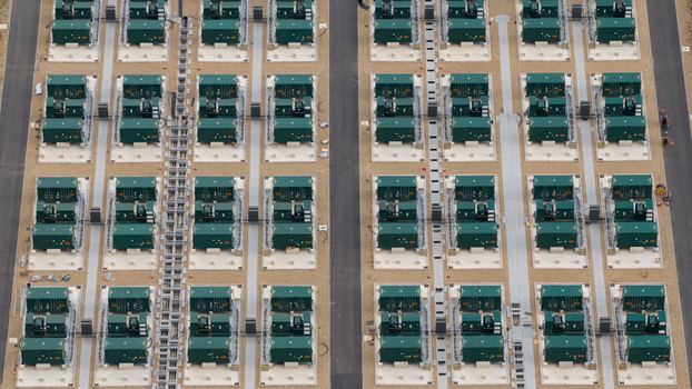 Aerial view of a large scale battery energy storage system with rows of green industrial containers on gravel pads and paved access paths in London England United Kingdom.