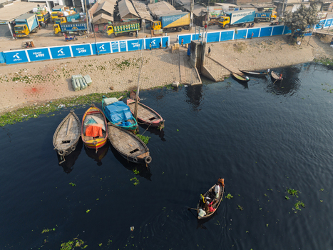Dhaka Division Bangladesh 23 January 2026 Aerial view of Buriganga River with traditional wooden boats docked along the embankment and trucks parked near the blue wall.