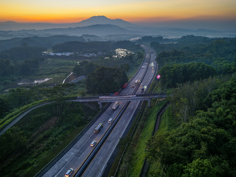 Aerial view of Jalan Tol Bawen Salatiga highway winding through lush green hills and rice fields at sunrise in Tengaran Central Java Indonesia. Aerial view of Jalan Tol Bawen Salatiga highway winding through lush green hills and rice fields at sunrise in Tengaran Central Java Indonesia.