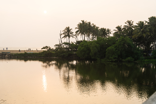 View of a tranquil lagoon reflecting the golden sunset with lush palm trees and people on the distant beach in Galle Southern Province Sri Lanka.