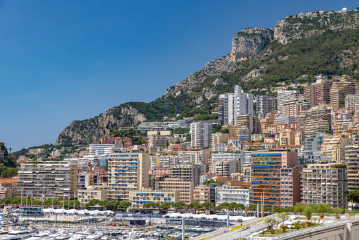View of the dense urban landscape of Monaco City with high rise residential buildings a bustling harbor filled with yachts and steep mountains in Monaco City Monaco. View of the dense urban landscape of Monaco City with high rise residential buildings a bustling harbor filled with yachts and steep mountains in Monaco City Monaco.