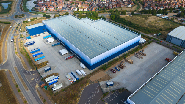 Aerial view of a large logistics warehouse facility with loading bays parked HGVs and trailers situated near a road network in Bedford England United Kingdom. Aerial view of a large logistics warehouse facility with loading bays parked HGVs and trailers situated near a road network in Bedford England United Kingdom.