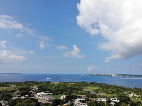 Aerial view of Sesoko Island featuring lush green vegetation coastal buildings and the expansive blue ocean under a clear sky in Motobu Okinawa Japan. Aerial view of Sesoko Island featuring lush green vegetation coastal buildings and the expansive blue ocean under a clear sky in Motobu Okinawa Japan.