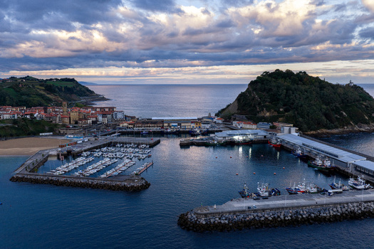 Aerial view of Getariako Portua with fishing boats docked in the marina surrounded by stone breakwaters coastal town buildings and green hills in Getaria Euskadi Spain.