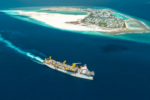 Aerial view of a large industrial vessel sailing through deep blue ocean waters towards the tropical island with white sand beaches and lagoons Vashafaru Haa Alif Atoll Maldives. Aerial view of a large industrial vessel sailing through deep blue ocean waters towards the tropical island with white sand beaches and lagoons Vashafaru Haa Alif Atoll Maldives.