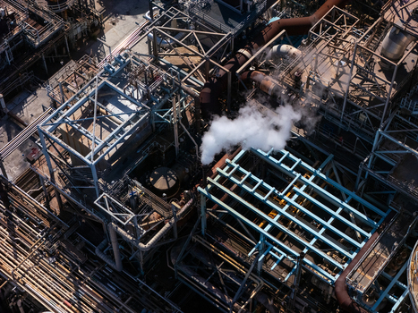 Aerial view of an industrial refinery complex with complex networks of pipes steel structures and steam rising from a vent in Carson California United States.