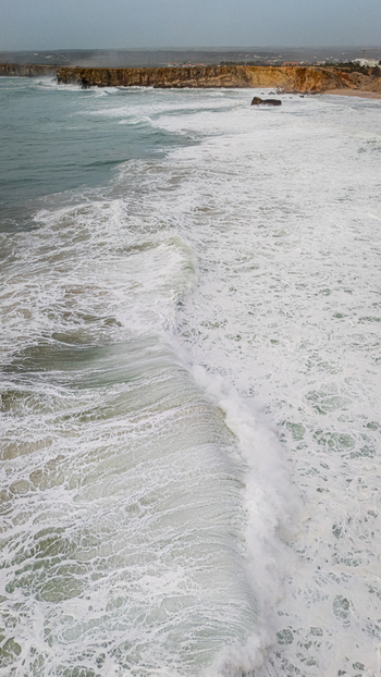 Aerial view of the powerful Atlantic waves crashing against the rugged golden cliffs of Sagres under an overcast sky Sagres Faro Portugal. Aerial view of the powerful Atlantic waves crashing against the rugged golden cliffs of Sagres under an overcast sky Sagres Faro Portugal.