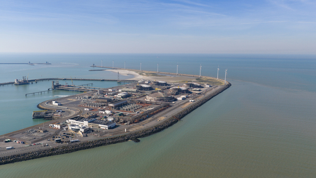 Aerial view of the Fluxys LNG Terminal Zeebrugge with large storage tanks and wind turbines along the coastline under a clear blue sky in Brugge Vlaanderen Belgium. Aerial view of the Fluxys LNG Terminal Zeebrugge with large storage tanks and wind turbines along the coastline under a clear blue sky in Brugge Vlaanderen Belgium.