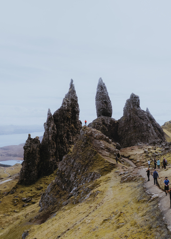 Aerial view of The Storr rock formations with hikers on the trail and rugged landscape under a cloudy sky in Portree Scotland United Kingdom. Aerial view of The Storr rock formations with hikers on the trail and rugged landscape under a cloudy sky in Portree Scotland United Kingdom.