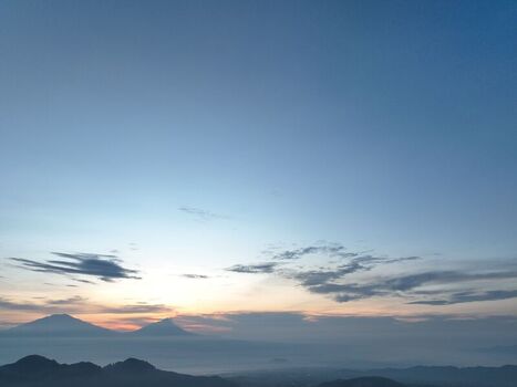 Aerial view of the mountainous landscape at sunrise with silhouettes of peaks and soft morning light over the valley in Kecamatan Kaliangkrik Jawa Tengah Indonesia. Aerial view of the mountainous landscape at sunrise with silhouettes of peaks and soft morning light over the valley in Kecamatan Kaliangkrik Jawa Tengah Indonesia.