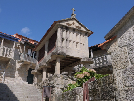 View of a traditional stone horreo granary with a cross on top surrounded by historic stone architecture and hydrangea flowers in Combarro Pontevedra Spain.