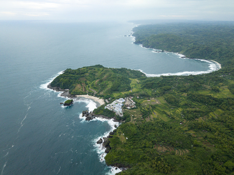 Aerial view of Jungwok Beach where the turquoise sea meets the verdant cliffs under a cloudy sky Gunungkidul Regency Special Region of Yogyakarta Indonesia. Aerial view of Jungwok Beach where the turquoise sea meets the verdant cliffs under a cloudy sky Gunungkidul Regency Special Region of Yogyakarta Indonesia.