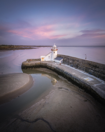 Aerial view of Balbriggan Harbour lighthouse at sunset with calm waters sandy beach and soft purple sky in Balbriggan County Dublin Ireland. Aerial view of Balbriggan Harbour lighthouse at sunset with calm waters sandy beach and soft purple sky in Balbriggan County Dublin Ireland.