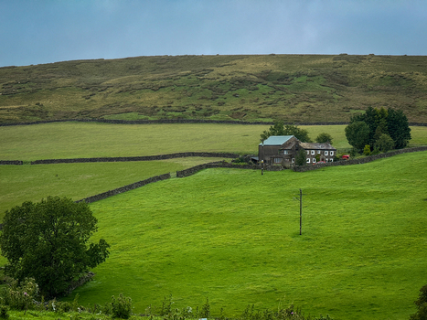 Yorkshire UK View of a traditional stone farmhouse nestled among vibrant green fields and dry stone walls on a rolling hillside under a cloudy sky. Yorkshire UK View of a traditional stone farmhouse nestled among vibrant green fields and dry stone walls on a rolling hillside under a cloudy sky.
