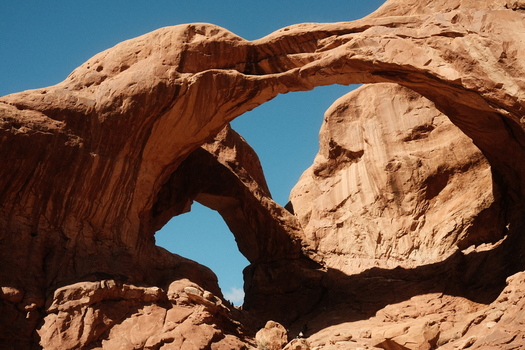 View of the massive red sandstone Double Arch formation under a clear blue sky in Arches National Park Grand County Utah United States. View of the massive red sandstone Double Arch formation under a clear blue sky in Arches National Park Grand County Utah United States.