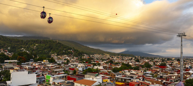 Aerial view of the cable car teleferico uruapan gliding over the dense urban landscape with rolling hills and a dramatic golden sunset sky above Uruapan Michoacan Mexico.
