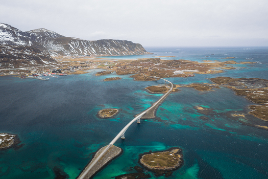 Aerial view of Flakstadbruene bridge connecting islands through the turquoise sea with snow capped mountains in the backdrop Flakstadbruene Nordland Norway. Aerial view of Flakstadbruene bridge connecting islands through the turquoise sea with snow capped mountains in the backdrop Flakstadbruene Nordland Norway.